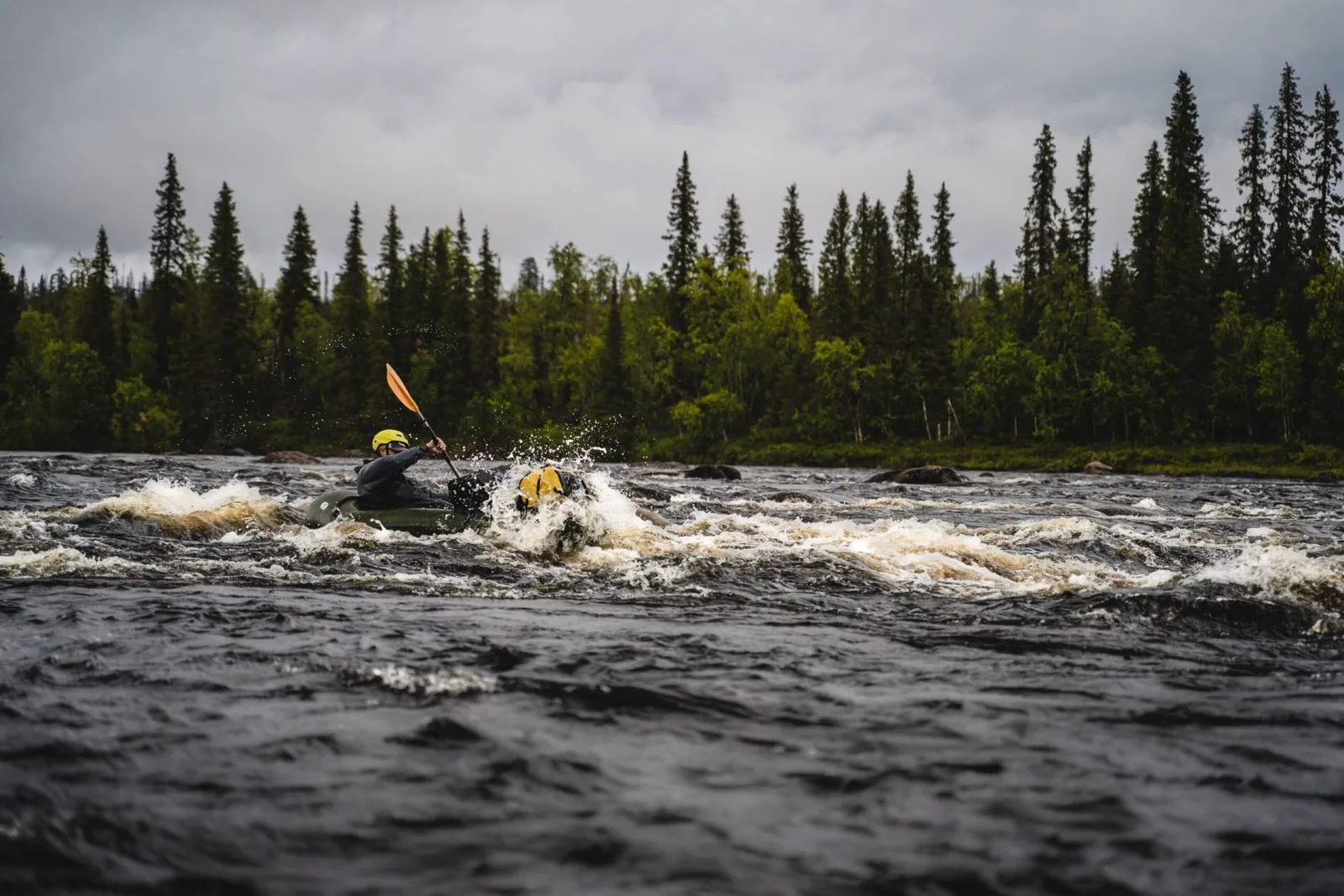 Une personne casquée descend une rivière agitée en packraft, au milieu de la forêt. Photo : PINPACK / packrafting.pl.