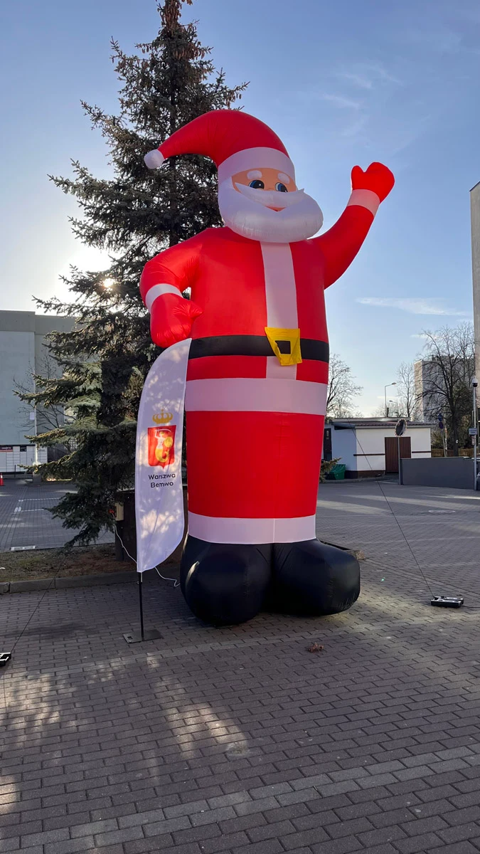 Inflatable Santa with a raised hand beside a Christmas tree — reference photograph